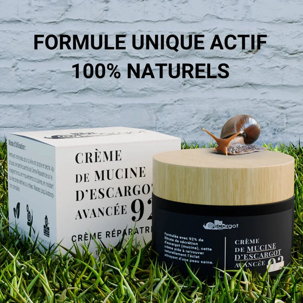 Pot de crème de mucine d'escargot avancée avec un couvercle en bois et une boîte d'emballage sur un fond d'herbe, accompagné d'un escargot, mettant en avant sa formule réparatrice 100% naturelle.